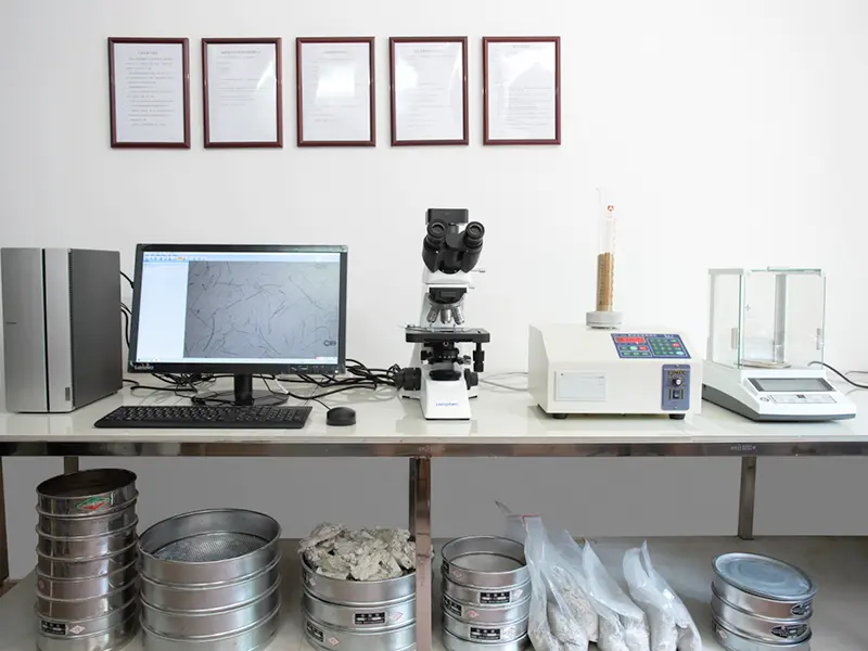 In-house testing lab: microscope, computer showing fibre microscopy image, particle-size analyzer and precision balance on the bench, certificates on the wall, sieve trays and sample bags below