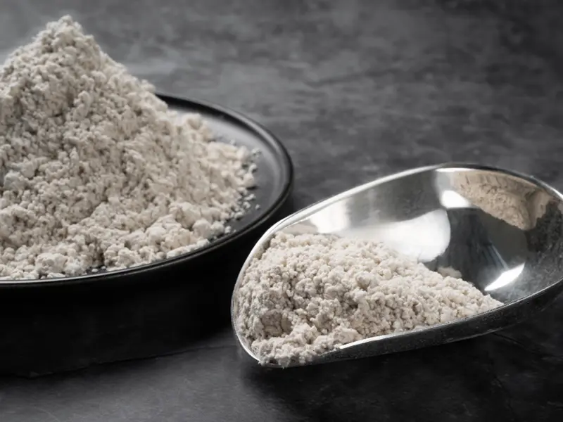 Off-white mineral fibre samples: a pile of off-white fibre powder on a black dish and the same fibre in a metal sampling scoop