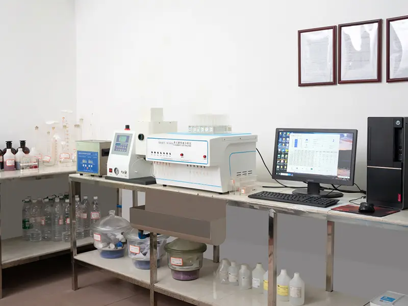 Chemical composition analysis lab: elemental analyzer, computer showing test data table, glassware and reagent bottles on the bench, certificates on the wall